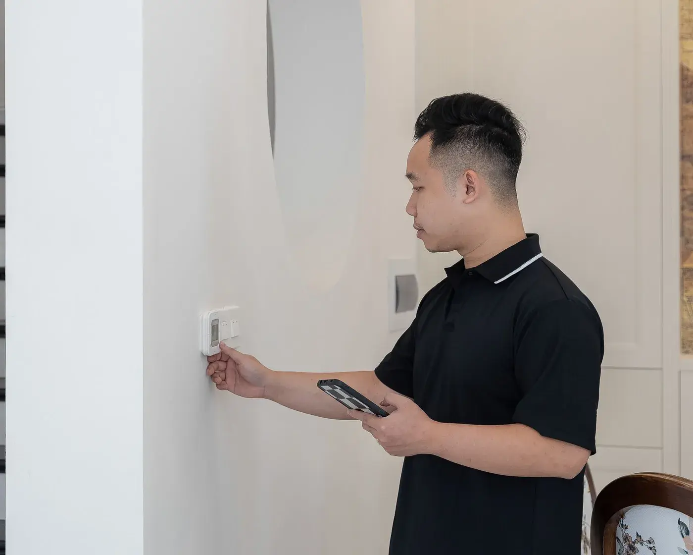 HVAC technician checking a wall thermostat in a customer's home, phone in hand